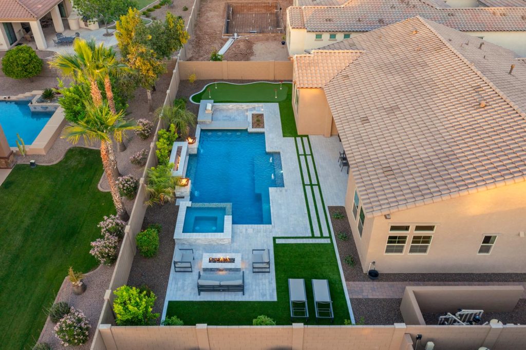 An aerial view of a house in Gilbert Arizona with a custom pool, fire pit area, and a putting green. The design emphasizes clean lines, and the pool area offers a cozy ambiance with lighting and seating.